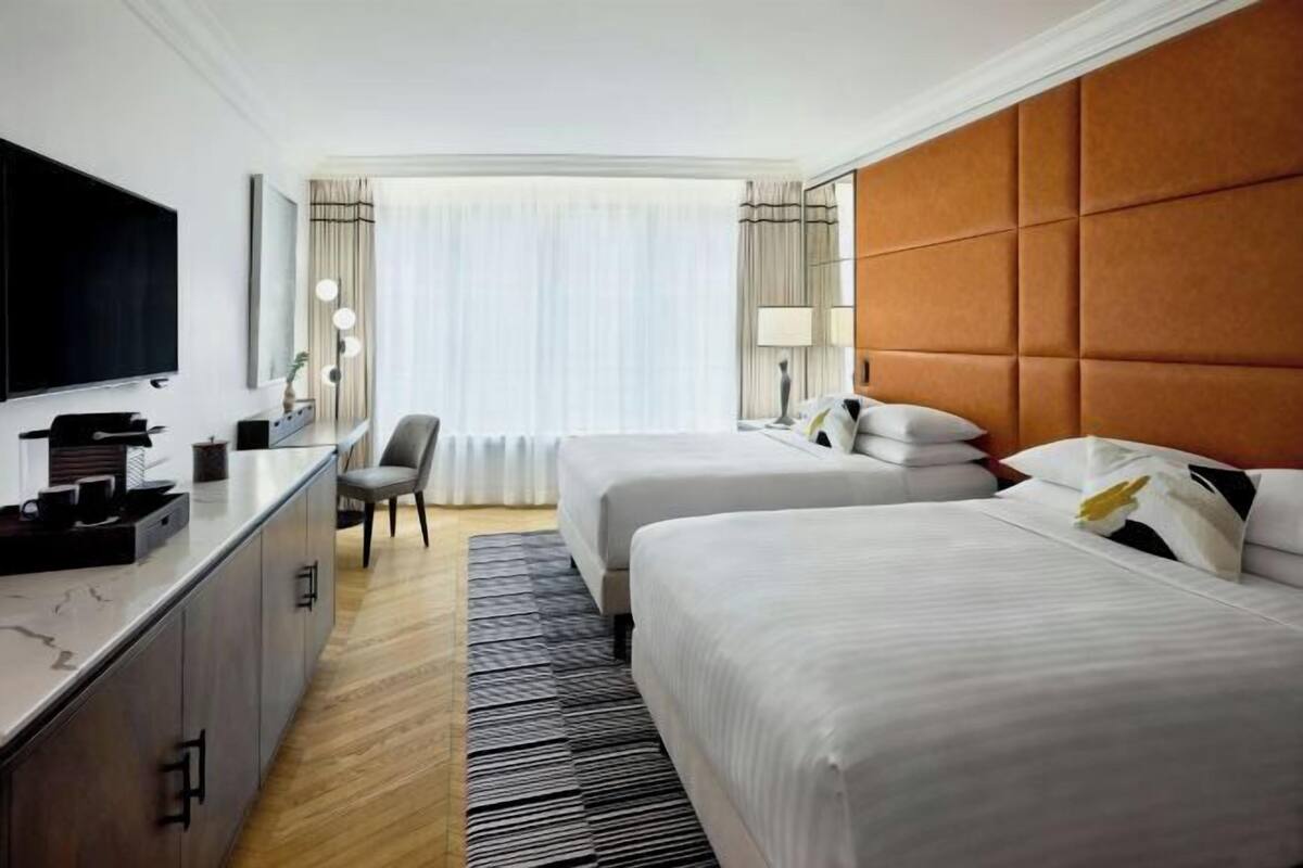 Una habitación de hotel con dos camas, televisión, escritorio y ventana con cortinas.
