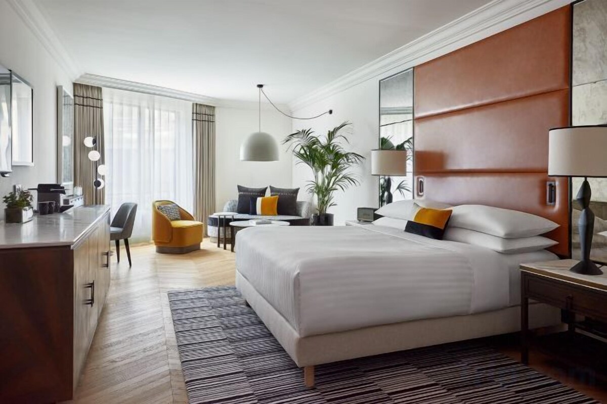 Una camera d'albergo con un letto grande, una scrivania, una sedia, una pianta e una finestra.