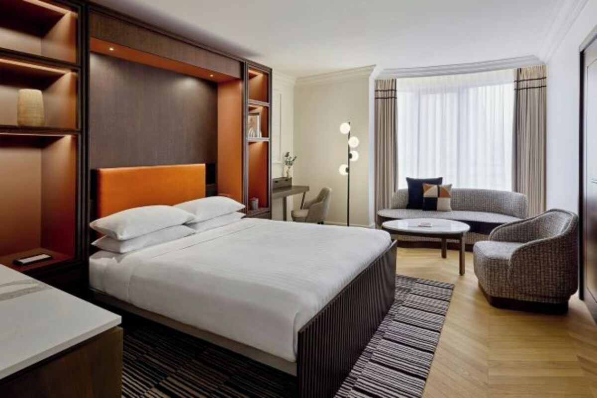 Een hotelkamer met een groot bed, een zithoek met een bank en fauteuils, een kleine tafel en een vloerlamp.