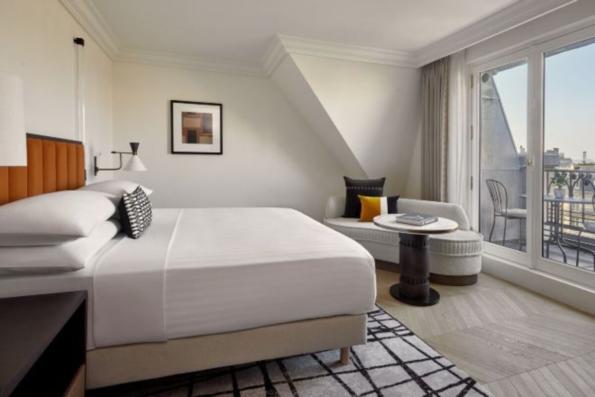 Une chambre d’hôtel moderne avec un grand lit, une petite table ronde et un balcon avec vue.