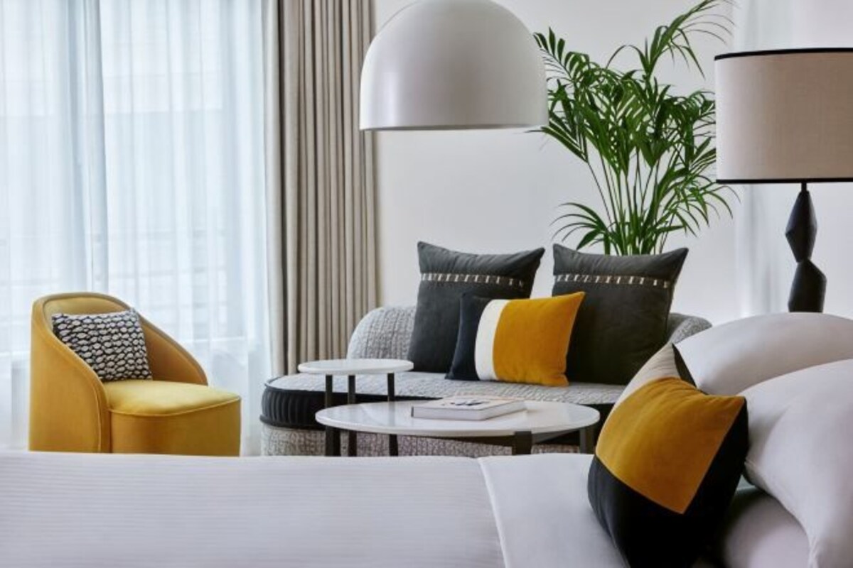 Een hotelkamer met een bed, een slaapbank, een klein rond tafeltje, een stoel en een lamp.