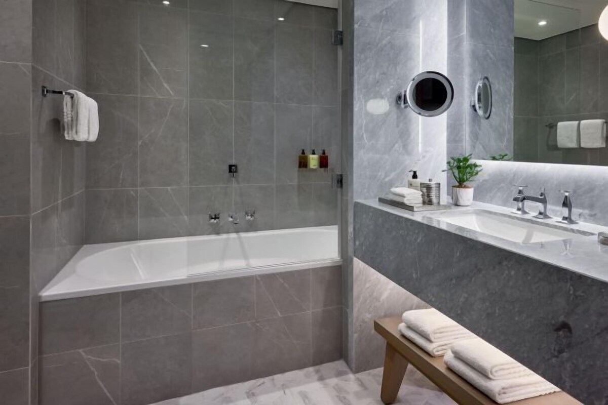 Ein modernes Badezimmer mit einer freistehenden Badewanne, einem Waschtisch mit Spiegel und einer Sitzbank mit Handtüchern.