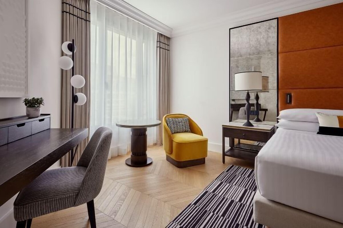 Une chambre d’hôtel moderne équipée d’un lit, d’un bureau, d’une chaise, d’une petite table et d’une lampe.