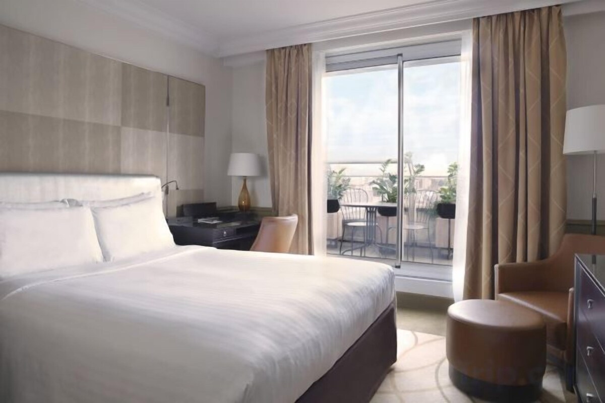 Una camera d'albergo con un letto grande, una scrivania, una sedia, una lampada e vista sull'esterno tramite una porta scorrevole.