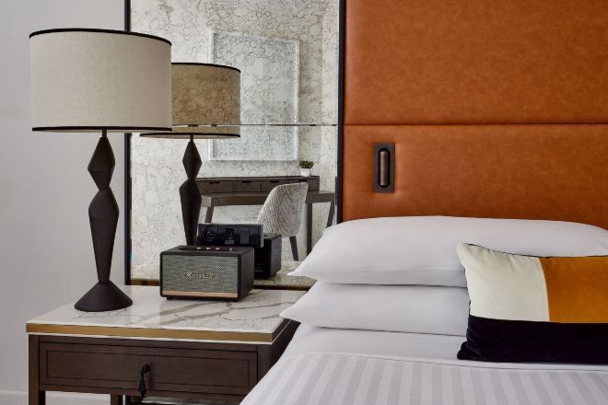 Een hotelkamer met een bed, een nachtkastje met een lamp, een radio en een wand met een marmerpatroon.