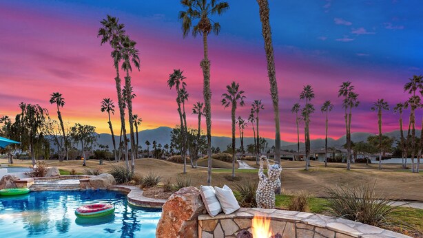 A swimming pool with a fire pit and inflatable rings, surrounded by palm trees and a sunset view. - 3 Bed Permit#227096 PGA West, relaxing heated pool home with views! (La Quinta)