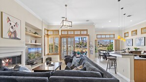A spacious living room with a fireplace, a large sofa, and a dining area with a view of the outdoors. - 3 Bed Permit#227096 PGA West, relaxing heated pool home with views! (La Quinta)