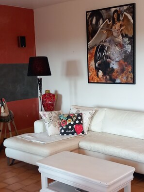 Una sala de estar con un sofá blanco, una mesa de centro, una lámpara, una obra de arte enmarcada y un cojín decorativo.
