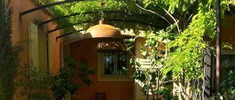 A courtyard with a stone pathway leading to a covered area, surrounded by potted plants and a building with a tiled roof.