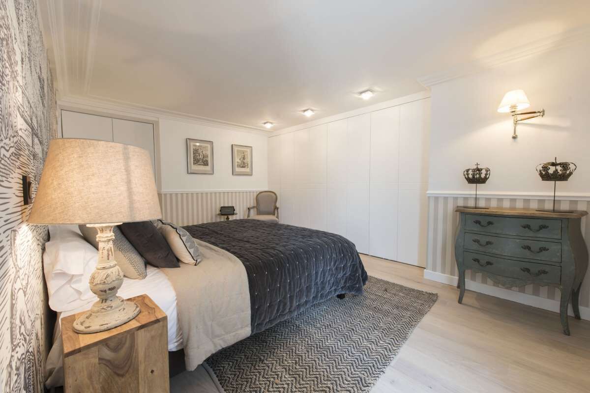 A bedroom with a bed, nightstand, lamp, dresser, and wall-mounted lights.