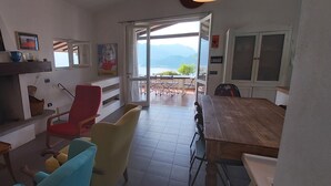 Ein Essbereich mit einem Holztisch, bunten Stühlen, einem roten Sessel und Bergblick durch eine offene Tür.