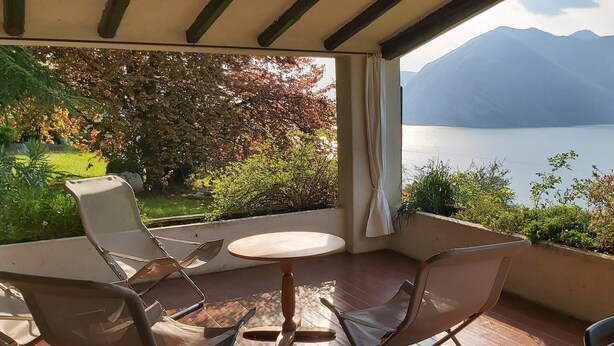 Ein Balkon mit Tisch und Stühlen mit Blick auf einen See und Berge.