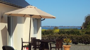 Una terrazza con tavolo e sedie, un ombrellone beige e vista sul mare.