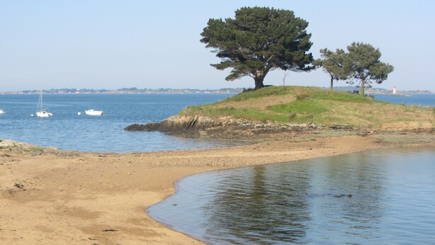 Una spiaggia con acque calme, una riva sabbiosa e alcune barche in lontananza.