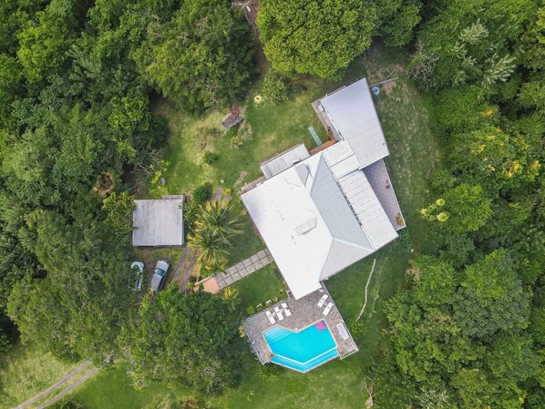 Vista aérea de una propiedad con piscina, garaje independiente y una casa grande con techo inclinado.