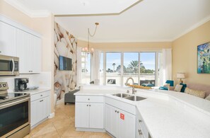 Una cocina moderna con armarios blancos, un lavamanos de acero inoxidable y un amplio ventanal con vistas a una palmera.