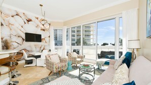 A modern living room with a large TV, comfortable seating, a dining area, and a balcony with a view of the city. - An updated, modern star on the Gulf Coast shoreline! 🌟 (Destin)