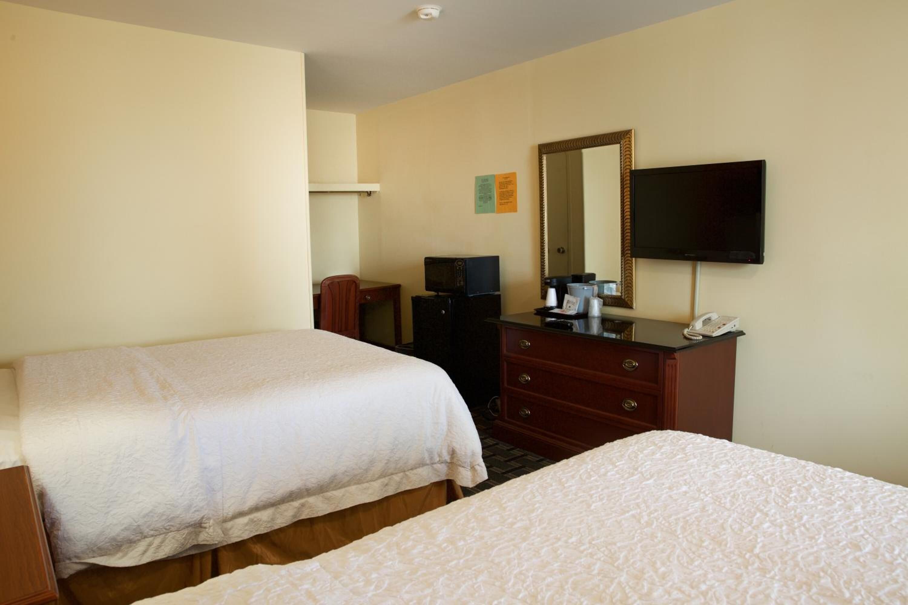 A hotel room with two beds, a TV, a dresser, and a mirror.