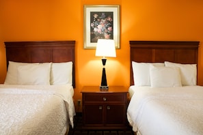 A hotel room with two beds, a nightstand with a lamp, and a framed floral artwork on the wall.