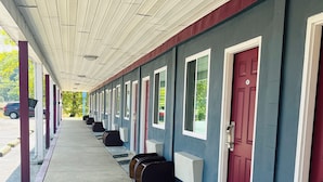 A row of motel rooms with individual doors, a covered walkway, and a parking area visible in the background. - Highlander Motel (Athens)
