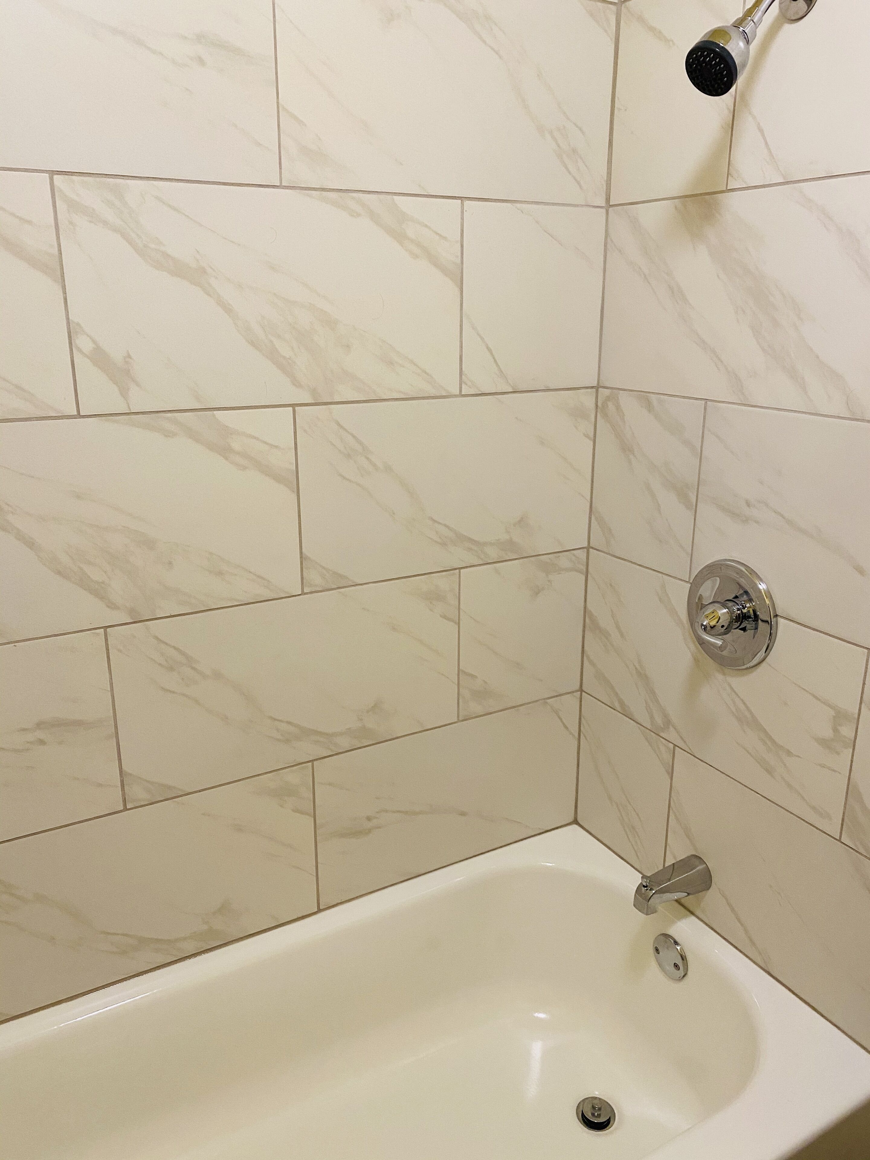 A bathroom with white marble tiles, a bathtub, and a shower head.
