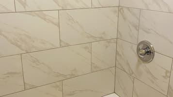 A bathroom with white marble tiles, a bathtub, and a shower head.