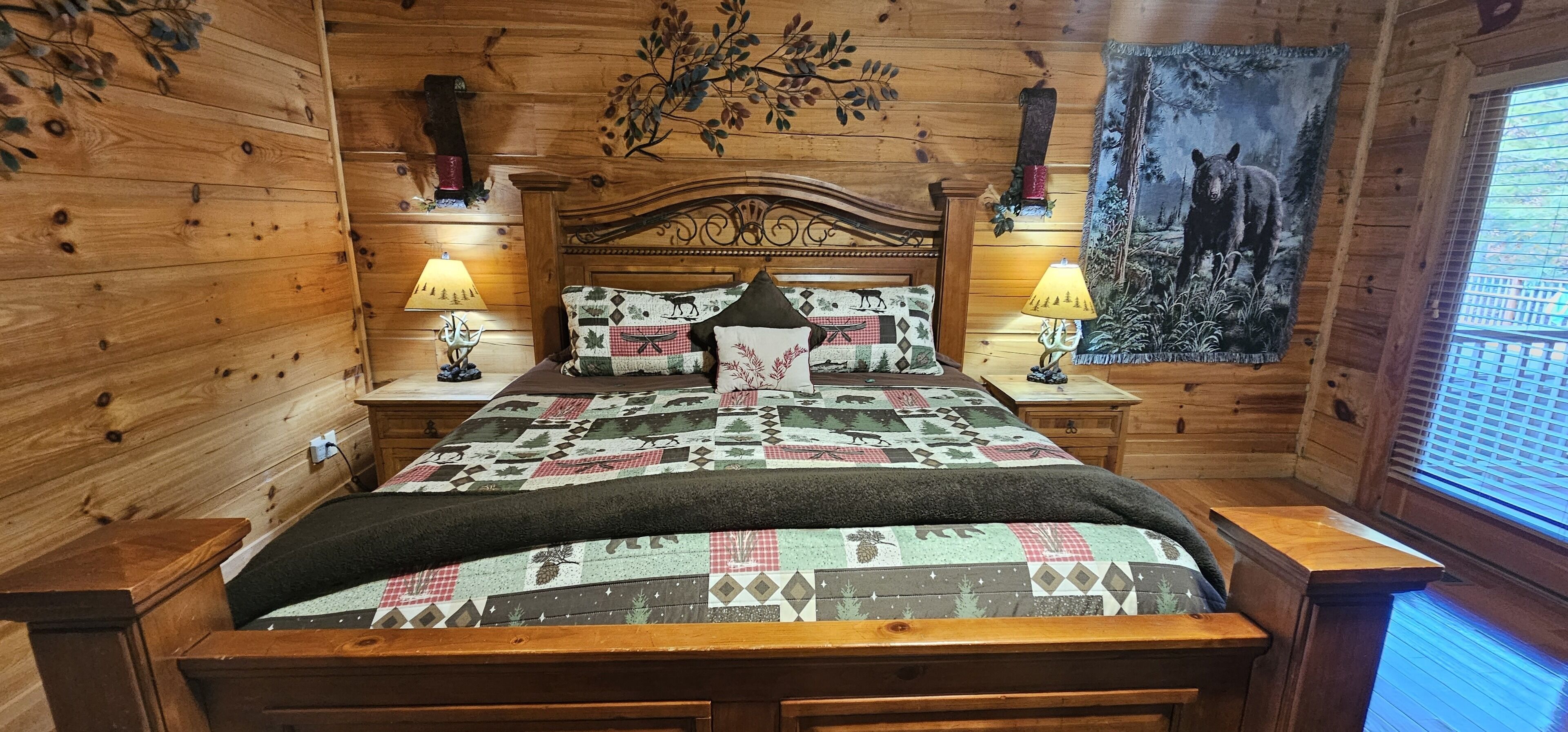Ein Schlafzimmer einer Holzhütte mit einem Bett, zwei Nachttischen, zwei Lampen und einer Wandteppich.