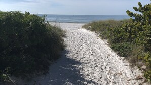 Een zandpad dat naar een strand leidt, met heldere lucht.