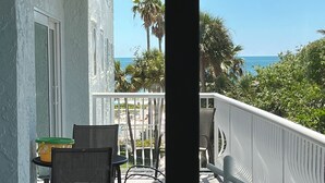 Een balkon met uitzicht op de oceaan, palmbomen en een stoel.