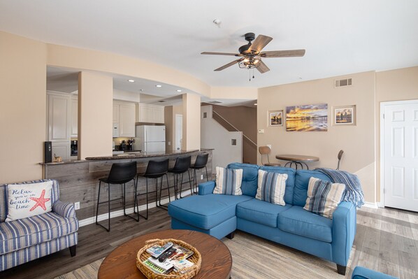A modern living room with a blue sectional sofa, a coffee table, and a bar area with stools.