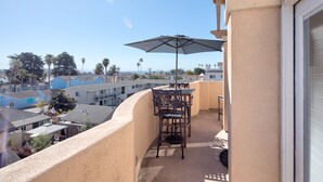 Ein Balkon mit Tisch und Stühlen, einem Sonnenschirm und Blick auf benachbarte Gebäude und Bäume.