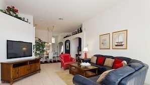 Una sala de estar con televisor, sofá y sillón rojo.