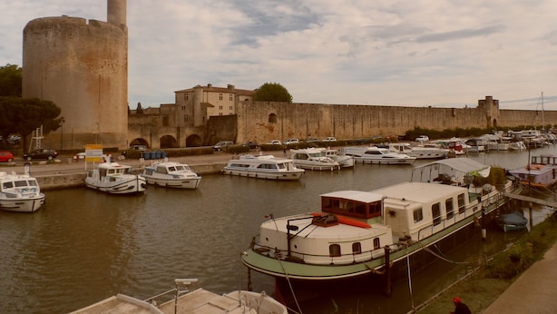A marina with boats docked, a large tower, and a historic building with a wall.