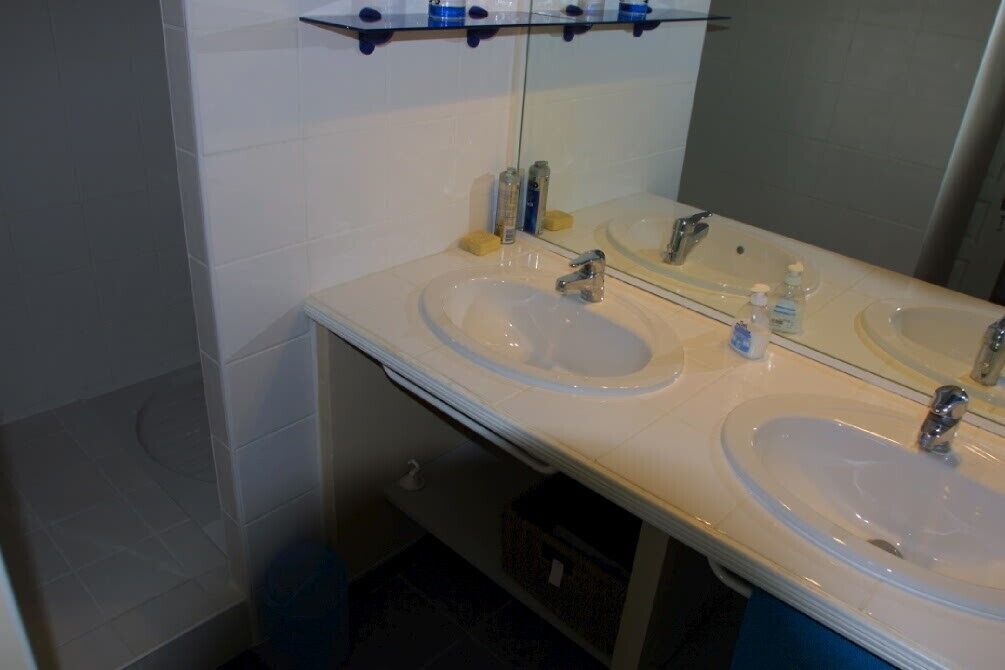 Une salle de bain avec deux lavabos, un miroir et une étagère au-dessus des lavabos.
