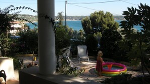 Un patio con vista al mar, una silla blanca y un niño jugando con un flotador de piscina.