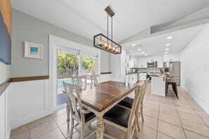 A modern kitchen with white cabinets, a central island, and a dining area with a wooden table and chairs.