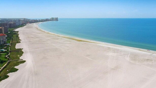 Eine Küstenstadtlandschaft mit einem breiten Sandstrand, Hochhäusern und blauem, wolkenlosem Himmel.
