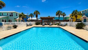 A rectangular swimming pool with clear blue water, surrounded by a white fence, and adjacent to colorful houses. - Shared Pool, Ample Parking, Golf Cart Access (Port Aransas)