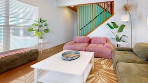 A modern living room with a white coffee table, a pink sofa, a green sofa, and a staircase with teal railings. - Shared Pool, Ample Parking, Golf Cart Access (Port Aransas)
