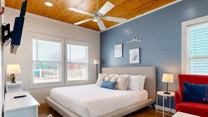 A bedroom with a bed, a red armchair, a ceiling fan, and a wall-mounted TV. - Shared Pool, Ample Parking, Golf Cart Access (Port Aransas)