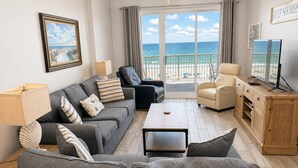 A living room with a sofa, chairs, a coffee table, a TV stand, and a balcony with a view of the ocean. - Beautiful Gulf Front ~ 2BD 2BA ~ 2 King Beds ~ 5th Floor ~ GulfShoresByOwner (Gulf Shores)