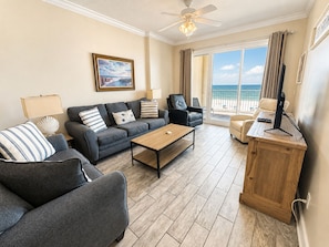 Un salon comprenant un canapé, des fauteuils, une table basse, un téléviseur et donnant sur la plage.