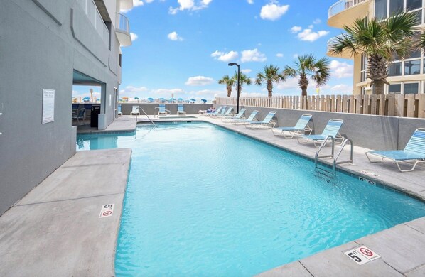 Relax by the pool surrounded by lounge chairs and a wooden fence.