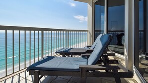 Un balcón con dos sillones azules y una mesa, con vista a una playa de aguas turquesas cristalinas.