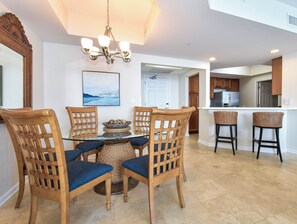 A dining area with a round glass table, four wooden chairs with blue cushions, a decorative bowl, and a chandelier. - 2BR 🌊Gulf Front🌊Silver Beach Towers West 1602 (Destin)