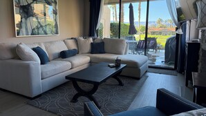 Una sala de estar con un sofá modular, una mesa de centro y un ventanal con vistas a un jardín y montañas.