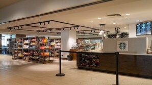 Un espace intérieur spacieux comprenant un comptoir de café, des étagères remplies de collations et un présentoir affichant le menu.