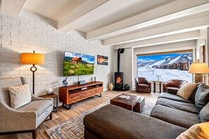A cozy living room with a fireplace, comfortable seating, a flat-screen TV, and a scenic view of a snowy landscape. - Slopeside, Sensational Ski Area Views, Pool, Hot Tub, Ski Locker, Ski-In (Steamboat Springs)