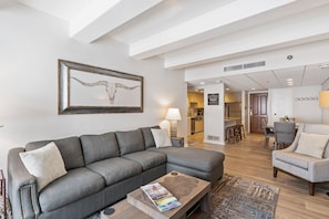 A modern living room with a grey sectional sofa, a coffee table, and a dining area in the background.