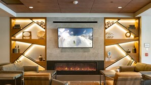 Un salon moderne doté d’un grand téléviseur à écran plat fixé au-dessus d’une cheminée, entouré d’étagères en bois et de sièges confortables.